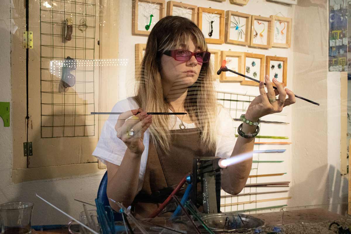 Γυναίκα κατασκευάζει γυάλινα κοσμήματα με φλόγιστρο στο εργαστήριό της.
