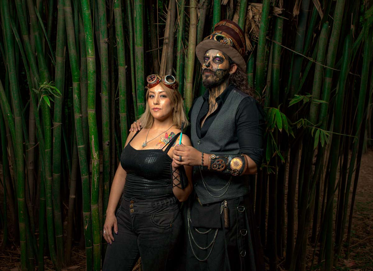 Δύο μεταμφιεσμένοι με steampunk στολές, καπέλα, μηχανικά αξεσουάρ και εντυπωσιακό μακιγιάζ ποζάρουν μπροστά σε μπαμπού.